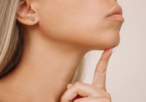 Close up side profile of a woman touching her chin, highlighting jawline definition and lower face contours.
